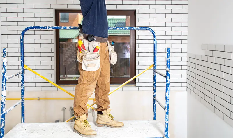 Peintre en bâtiment sur échafaudage intérieur, travaux de rénovation