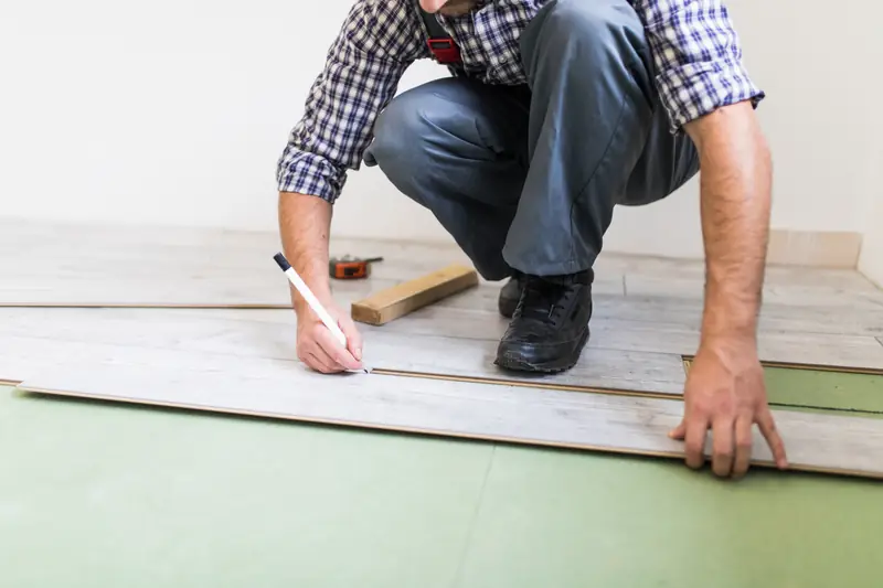Pose de parquet stratifié — artisan traçant un repère de coupe sur lame de bois