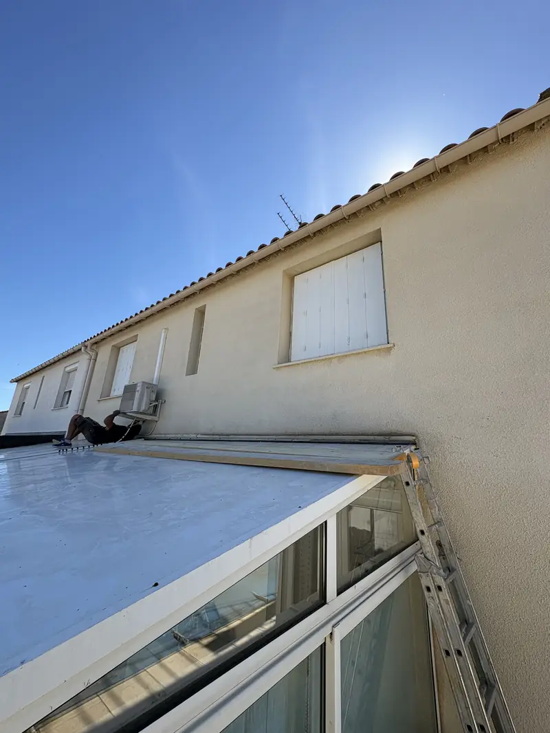 Façade à rénover à Béziers — mur crépi vieilli au-dessus d'une véranda, travail en hauteur à l'échelle