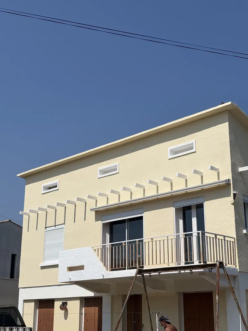 Ravalement de façade terminé à Béziers — maison enduite en jaune pâle avec balcon et génoises blanches