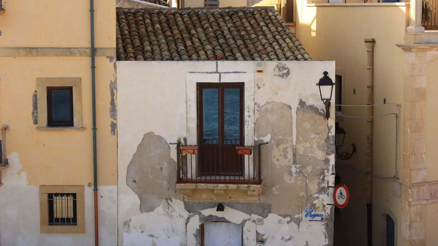 Façade ancienne au crépi dégradé avec balcon, bâti méditerranéen nécessitant un ravalement